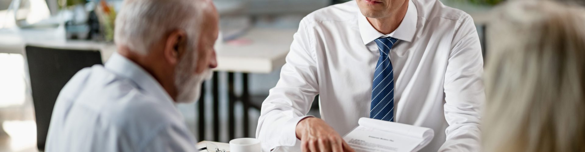 Insurance agent having a meeting with senior clients and pointing at place of the signature on a contract.