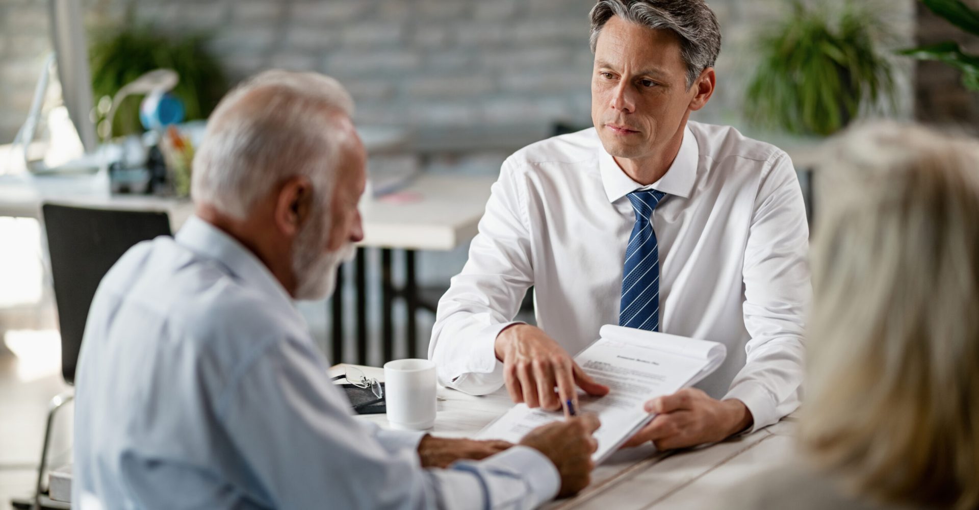 Insurance agent having a meeting with senior clients and pointing at place of the signature on a contract.